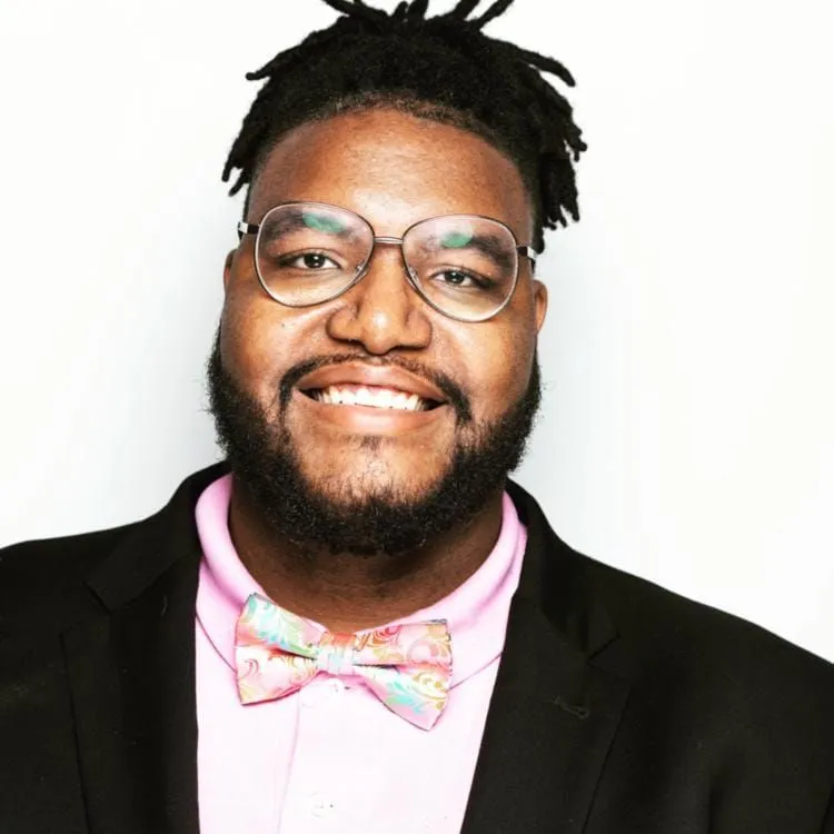 PG Brown smiling in a black tuxedo jacket, pink shirt, and patterned bow tie