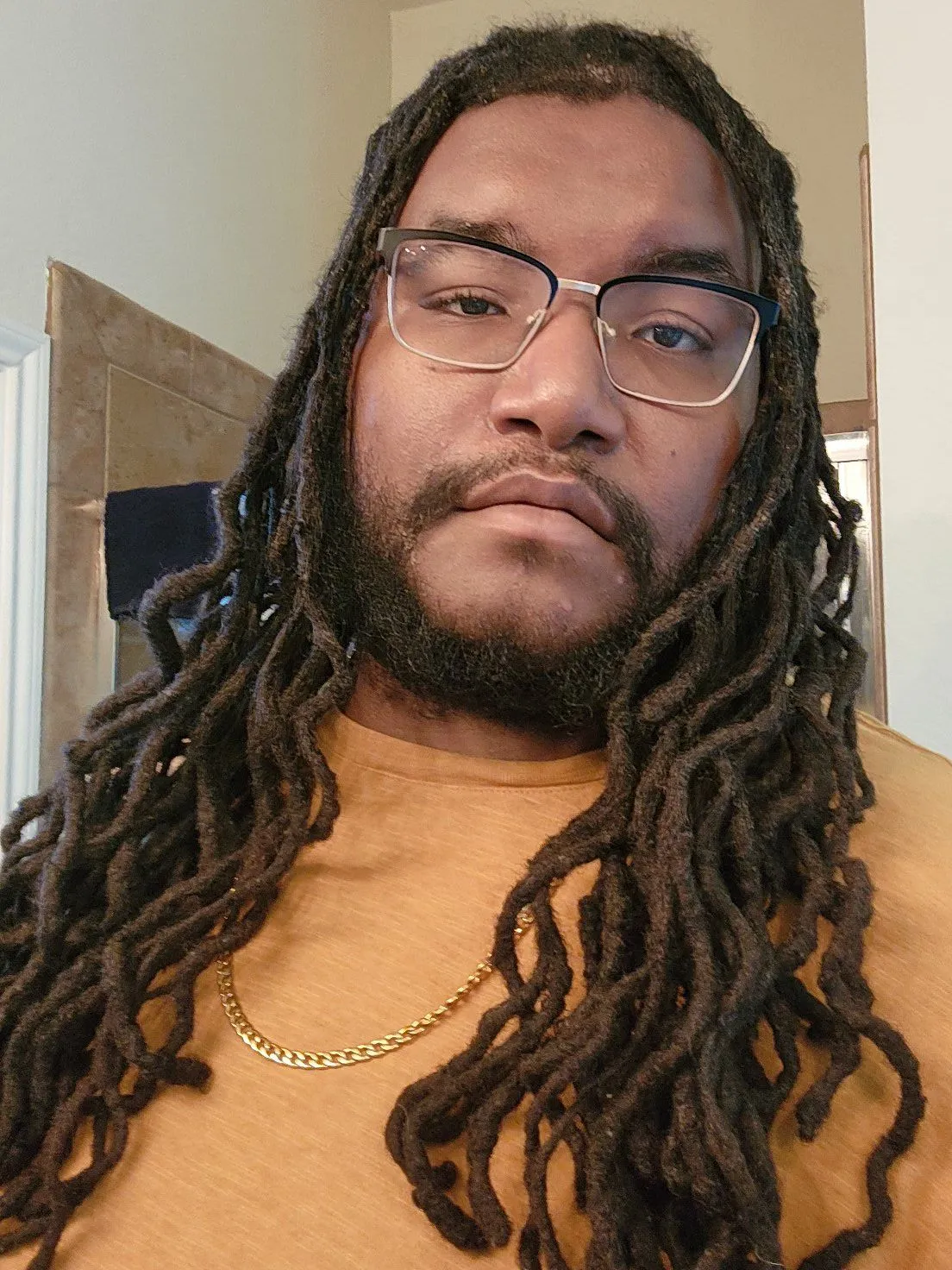 PG Brown smiling softly in glasses and a warm tan shirt