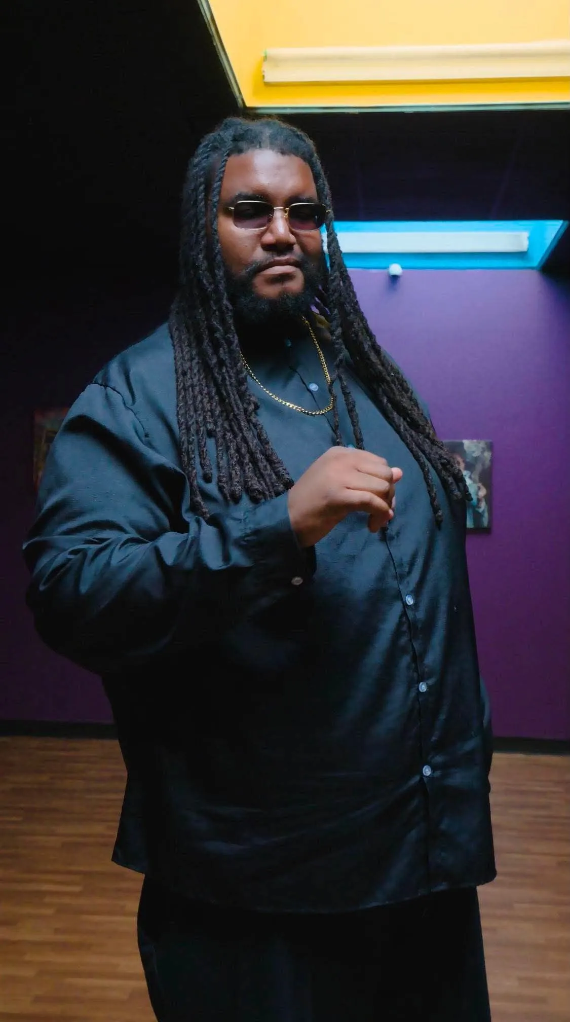 PG Brown standing in a colorful event space wearing a black shirt and gold chain